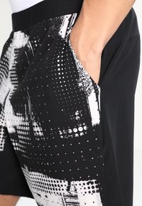 Schwarze Shorts mit einem strukturierten Design, das eine Mischung aus weißen Punkten und abstrakten Mustern aufweist. Enthält Seitentaschen und einen elastischen Bund.