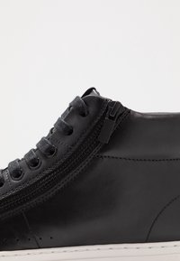 Czarne skórzane trampki z szarymi sznurówkami, bocznym zamkiem błyskawicznym, gładką teksturą i białą gumową podeszwą. Szczegółowe szwy wzdłuż krawędzi.