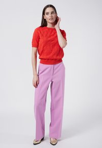 Suéter de punto rojo brillante con patrones texturizados, combinado con pantalones de tiro alto color lavanda y zapatos dorados. Diseño sencillo y moderno.
