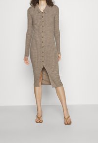 Lång, ribbad klänning med krage, knäppning fram och hög slits vid låret. Tillverkad av ett strukturerat, brunt tyg.