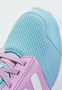 Jasnoniebieski sneaker z siateczkową cholewką, pastelowo różowe akcenty i białe logo. Gładkie tekstury i okrągły kształt z sznurowadłami z przodu.