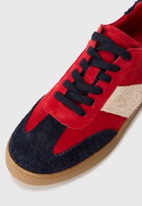Røde og marineblå semskede sneakers med en teksturert tan-accent, sorte snøringer og en gummisåle med et sikksakkmønster på overdelen.