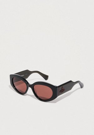 Gafas de sol negras con forma de ojo de gato redondeada, lentes de color rojo y una montura de plástico lisa. Presenta un acento de logo en la pata.