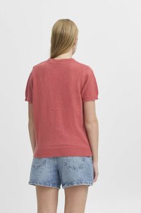 Kortärmad, korallfärgad stickad tröja med ribbad krage, kombinerad med ljusblå denimshorts med fransar och bakfickor.