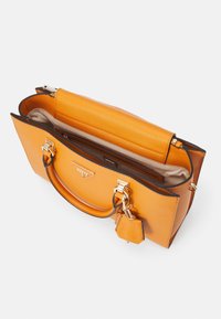 Pomarańczowa skórzana torebka o konstrukcyjnym designie, złote okucia, górna rączka oraz odczepiana zawieszka. Wnętrze wyściełane beżową podszewką.