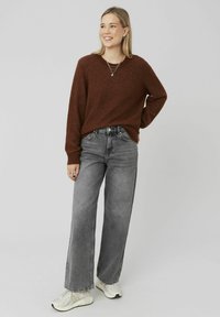 Un pull en tricot marron à manches longues, associé à un jean large taille haute gris et des baskets de couleur neutre. Bijoux superposés simples en accent.