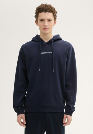 Sudadera azul marino con un bolsillo delantero, capucha con cordón y texto del logo en blanco. Hecha de tela suave con un ajuste relajado y puños acanalados.