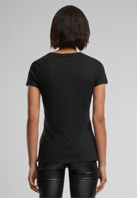 Svart tettsittende t-skjorte med korte ermer, rund hals og glatt stoff. Bært med svarte skinnende leggings. Ingen synlige mønstre eller logoer.