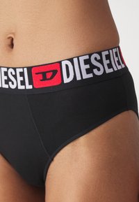 Svart bomullstruser med en fremtredende, flerfarget elastisk midjebånd som viser "DIESEL"-logoen i hvit og rød skrift.