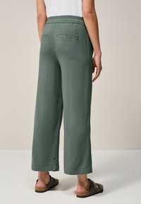 Pantalons larges verts à la coupe décontractée, avec une taille élastique et deux poches arrière. Texture lisse et design à longueur complète.