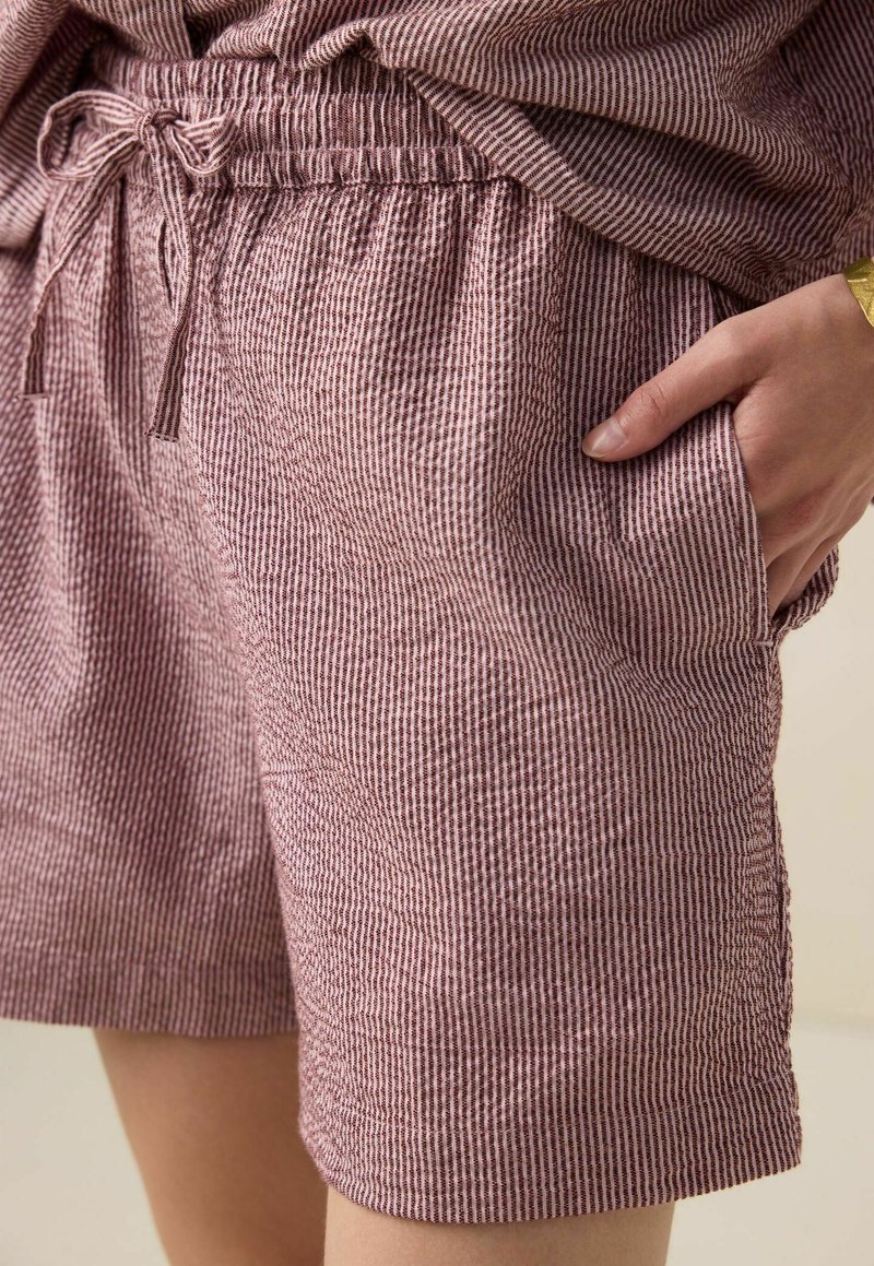 Shorts rayés rouges et blancs en tissu texturé avec une taille élastique et un cordon de serrage. Comprend des poches latérales pour le rangement.