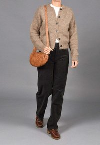 Cárdigan de punto marrón con botones, blusa blanca, pantalones de pana negros y bolso de cuero marrón. Zapatos marrones con suela texturizada.