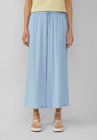 Lichtblauwe wijde broek van zachte stof, met een elastische tailleband en een koord. Gecombineerd met crèmekleurige sandaaltjes met bandjes.