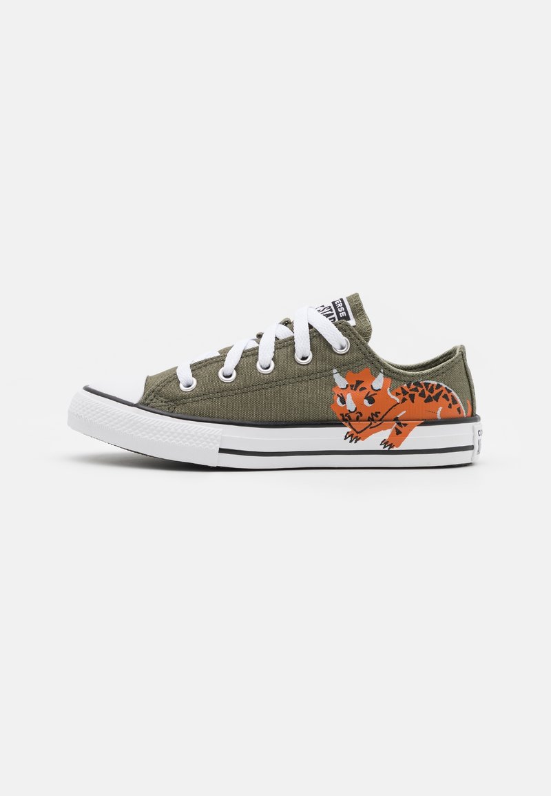 Baskets basses en toile vert olive avec lacets et semelle blancs, avec un tricératops orange dessin animé imprimé sur le côté.