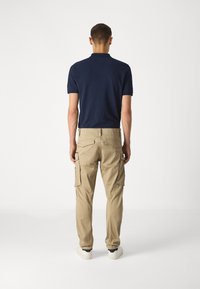 Marinblå polo och beige cargobyxor, med flera sidofickor och en avslappnad passform. Vita sneakers fulländar looken.