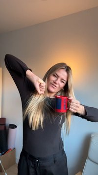 Rdeči keramični lonček z modrimi in rdečimi poudarki; model nosi črno majico, z dolgimi lasmi in igrivim izrazom na obrazu, medtem ko drži lonček.