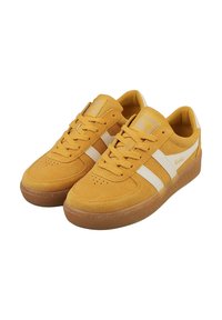 Zapatillas de ante amarillas con rayas blancas, cuello acolchado y suela de goma. Presenta perforaciones en la puntera para transpirabilidad y detalles del logo.