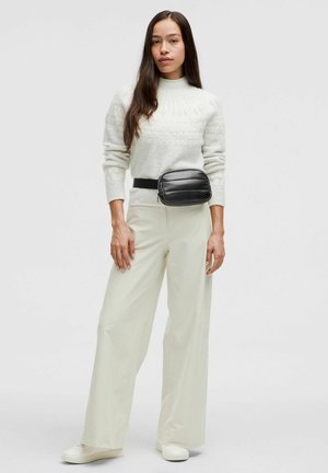 Hvid sweater med struktureret mønster, cremefarvede vidde-bukser og en sort puffy bæltetaske. Hvide sneakers fuldender outfittet.