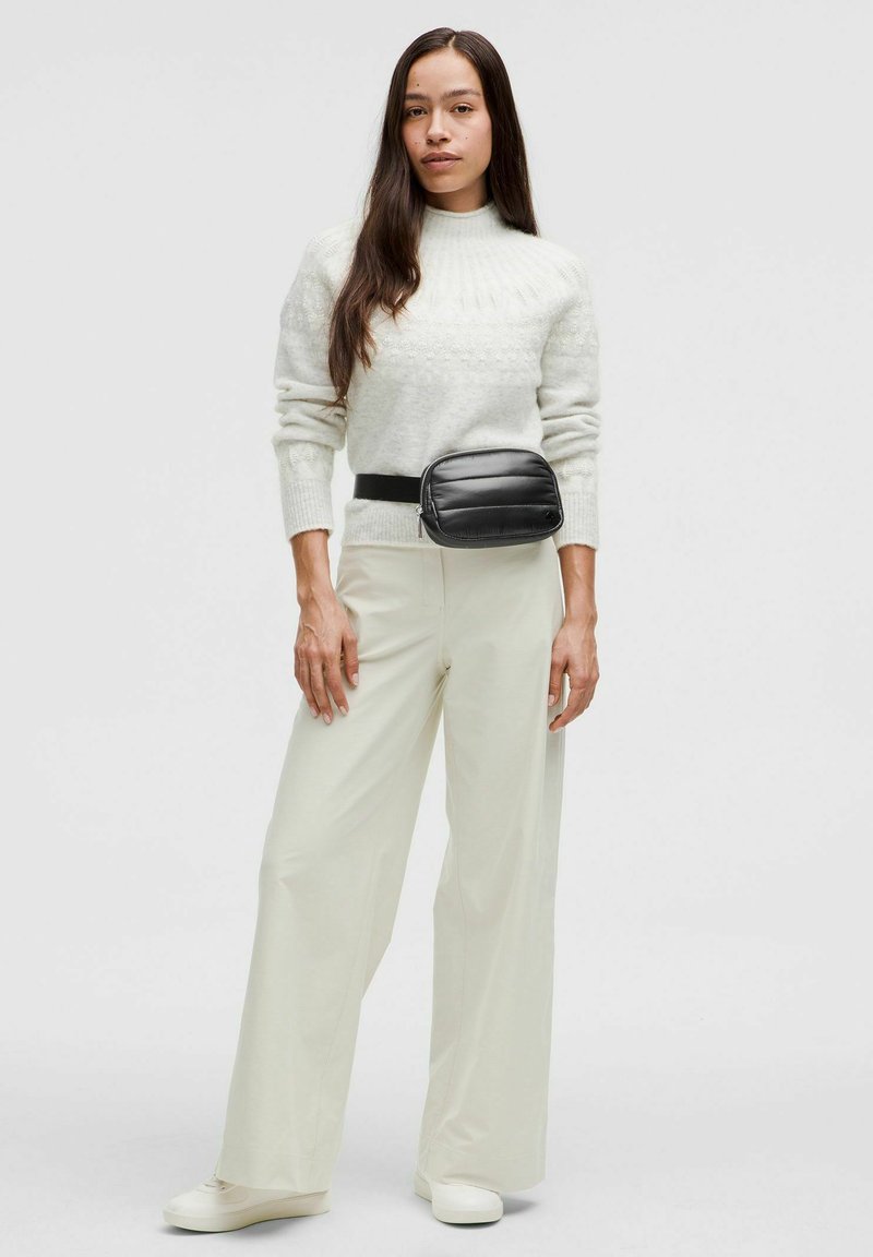 Fehér pulóver texturált mintával, krémszínű bő szárú nadrág és fekete puffos övtáska. A fehér sportcipők teszik teljessé az öltözéket.