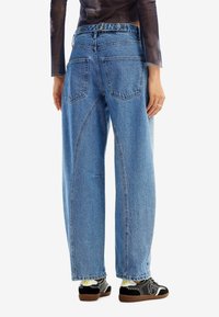 Ljusblå, högmidjade, vida jeans med fem fickor och en lätt sliten look. Bärs med svarta sneakers med vita detaljer.