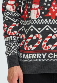 Grey knit sweater featuring holiday patterns: red snowmen, trees, candy canes, and text "MERRY CHRISTMAS." Ribbed cuffs and hem.