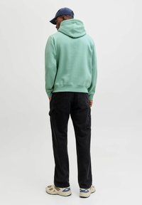 Menta zeleni dukserica s kapuljačom i opuštenim krojem, uparena s crnim cargo hlačama s bočnim džepovima i bež tenisicama s plavim detaljima.