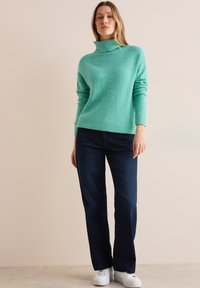 Suéter de cuello alto turquesa con un patr�ón texturizado, combinado con jeans rectos azul oscuro y zapatillas blancas. Atuendo simple y casual.