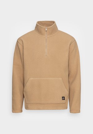 Pull polaire beige avec col à demi-fermeture éclair, manches longues et poche kangourou à l'avant, conçu pour la chaleur et un port décontracté.