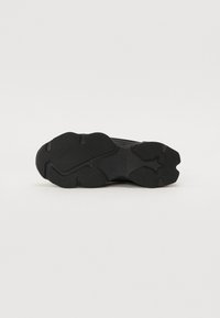 Black athletic shoe outsole with textured rubber for grip, featuring a smooth, curved design and distinctive tread pattern.