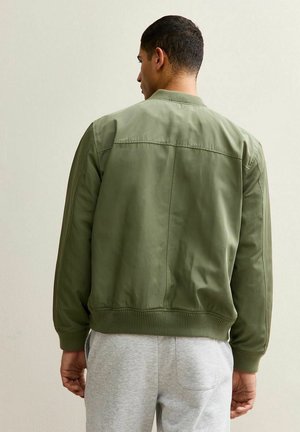 Olivgrüne Bomberjacke mit glatter Textur, gerippten Bündchen und Saum sowie klassischer Silhouette. Verfügt über ein minimalistisches Design und keine sichtbaren Metallteile.