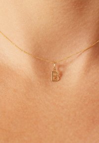 Gouden halsketting met een hanger in de vorm van een hoofdletter 'B'. De ketting is fijn en delicaat met een gladde textuur.