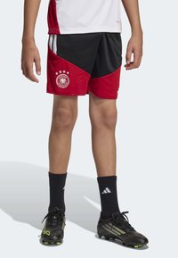 Red and black soccer shorts with a textured pattern, featuring a Germany logo and stars. Worn with black soccer socks and cleats.