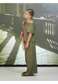 Top off-shoulder verde oliva e pantaloni larghi coordinati; dettaglio a scacchi rosso e bianco; scarpe basse grigie; morbido tessuto di cotone.
