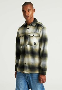 Camicia in flanella a maniche lunghe con bottoni, in un motivo plaid verde, nero e bianco; presenta due taschini sul petto, bottoni neri e colletto.