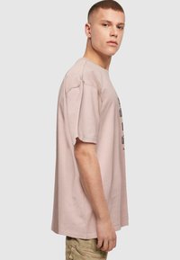 Lyserød oversized bomulds T-shirt med korte ærmer, som har fed sort tekst på forsiden. Enkel, udekoreret design med en afslappet pasform.