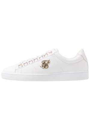 Witte lage sneaker met gouden veterogen, witte veters en een gouden decoratief logo aan de zijkant.