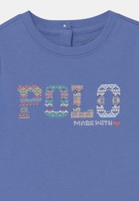 Niebieska bawełniana koszulka z okrągłym dekoltem, zdobiona kolorowym, dzianinowym logo "POLO" oraz napisem "MADE WITH" z akcentem serca.