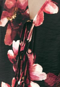 Abito floreale caratterizzato da grandi fiori rosa e bianchi su uno sfondo scuro, con un profondo scollo a V e lacci decorativi sul colletto. Tessuto texturizzato.