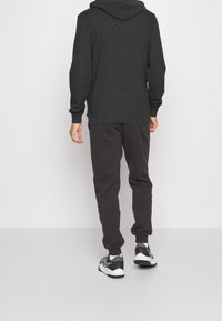 Sudadera negra con capucha y corte relajado, combinada con pantalones de chándal gris oscuro. El conjunto presenta puños acanalados y un diseño simple.