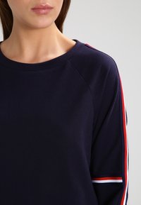 Marineblaues Sweatshirt mit Rundhalsausschnitt und Raglanärmeln. Mit rot-weißen und blauen Streifen an den Ärmeln und weichem Material.
