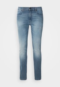 Jean slim bleu clair avec légère décoloration et whiskering, fermeture à boutons à l'avant et design cinq poches.