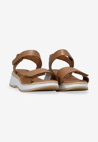 Sandalias de piel marrón con correas ajustables, puntera abierta, entresuela blanca y parte superior texturizada. Suela plana con un ligero relieve para mejorar la tracción.