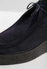 Chaussure en daim bleu marine avec un bout rond, des coutures apparentes, et une semelle plateforme noire texturée. Dotée d'un lacet à nouer sur le dessus.