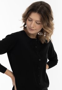 Cardigan negru din material moale, cu guler rotund, mâneci lungi și închidere cu nasturi negri.