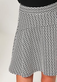 Gonna a righe bianco e nero con una vita aderente e un design svasato, caratterizzata da forme geometriche su tutto il tessuto.