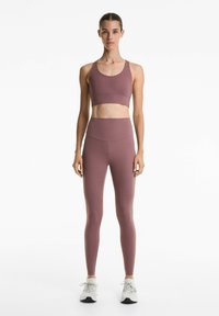 Mauve sportbeha en high-waisted legging van rekbaar materiaal. Heeft een gladde textuur en minimale naden, gecombineerd met lichte sportschoenen.