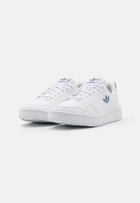 Weiße Ledersneaker mit einer strukturierten Gummisohle, blauen Logoakzenten, flachen Schnürsenkeln und durchbrochener Gestaltung an den Seiten.
