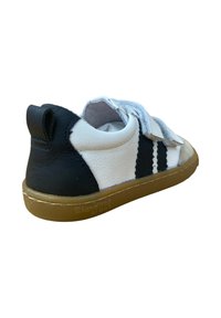 Zapato de cuero negro y blanco con suela de goma, que presenta correas de Velcro y costuras decorativas. Parte trasera redondeada con una pequeña pestaña para tirar.