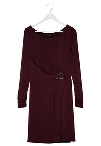 Burgundowa sukienka z długim rękawem z marszczonym przodem, asymetrycznym fasonem zapinanym z boku oraz detalem w postaci paska z metalową klamrą. Gładka textura materiału.