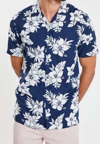 Tummansininen lyhythihainen paita valkoisella trooppisella kukkakuvioinnilla, jossa on kaulus ja napillinen etu.